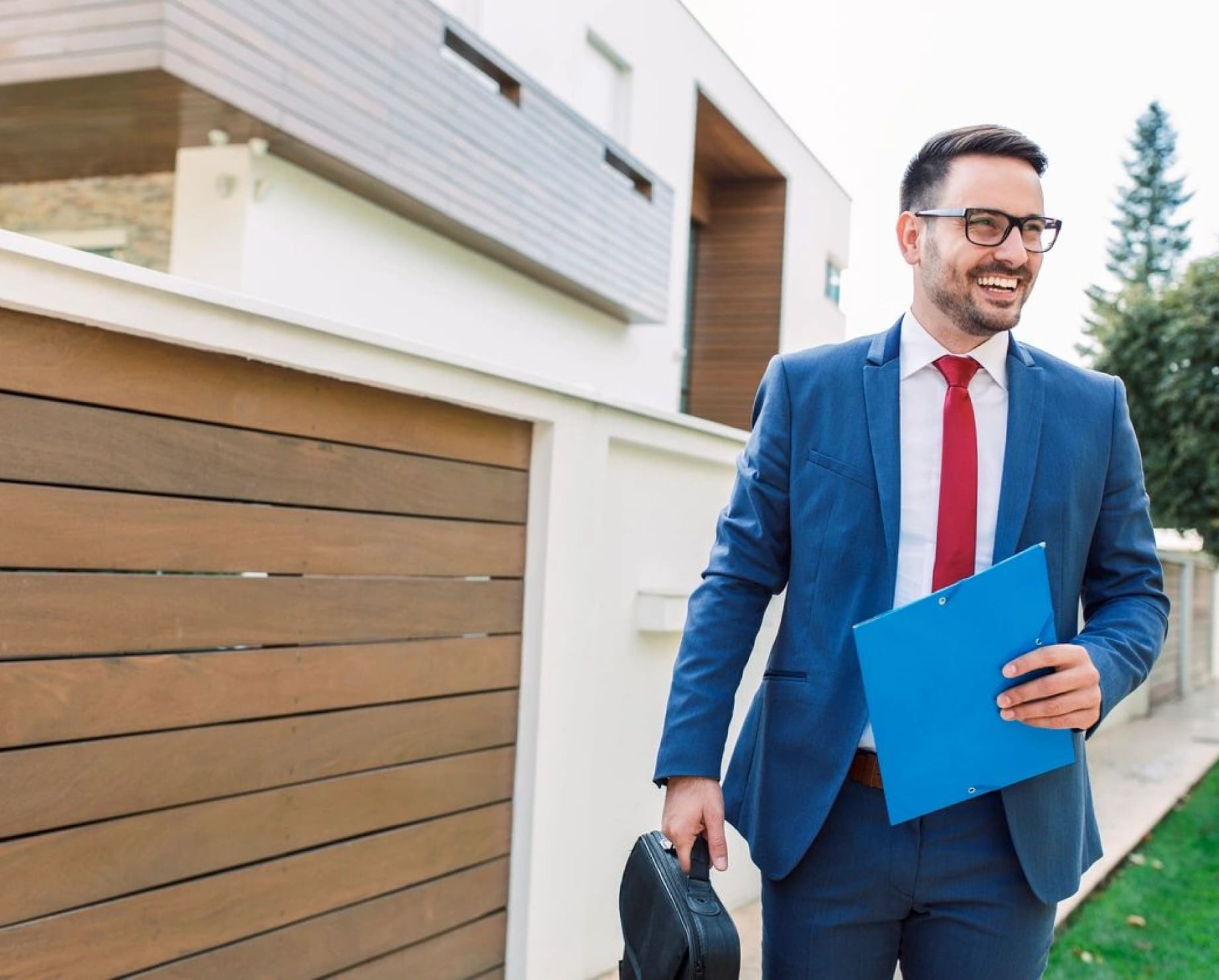 A man in a suit and tie holding a blue folder.