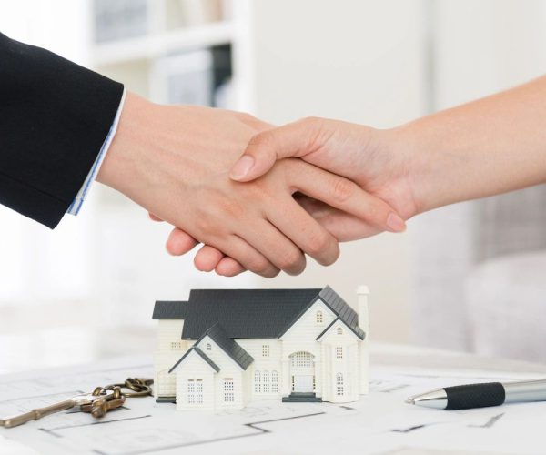 A man and woman shaking hands over a house.